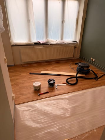 Delvis lagt trägolv med underlag, verktyg och dammsugare. Delvis lagt trägolv med underlag, verktyg och dammsugare.