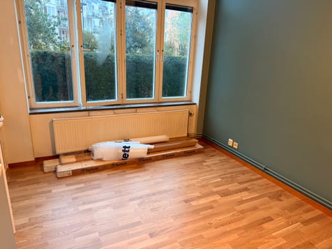 Lagt trägolv framför fönster och grön vägg, med kvarvarande material vid elementet. Lagt trägolv framför fönster och grön vägg, med kvarvarande material vid elementet.